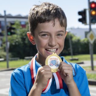 Kind mit goldener Medaille vor Ampel