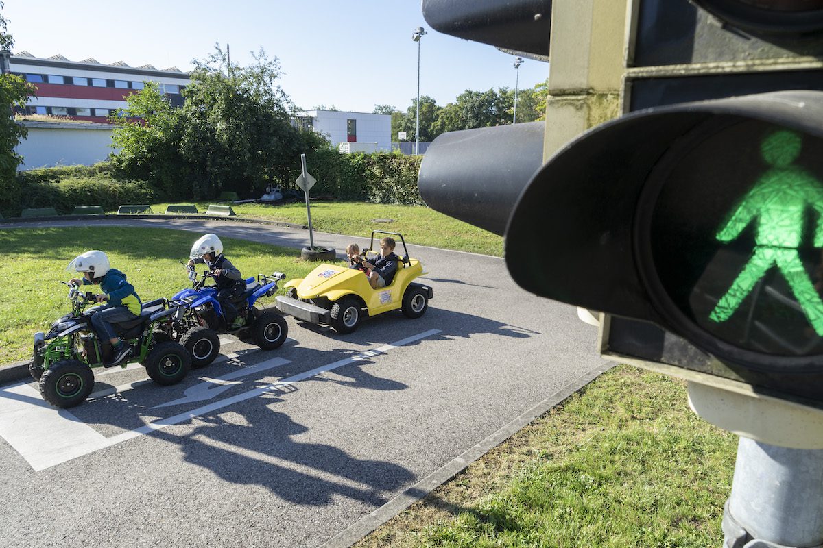 Grüne Fußgängerampel mit Kinderfahrzeugen im Hintergrund auf Verkehrsübungsplatz