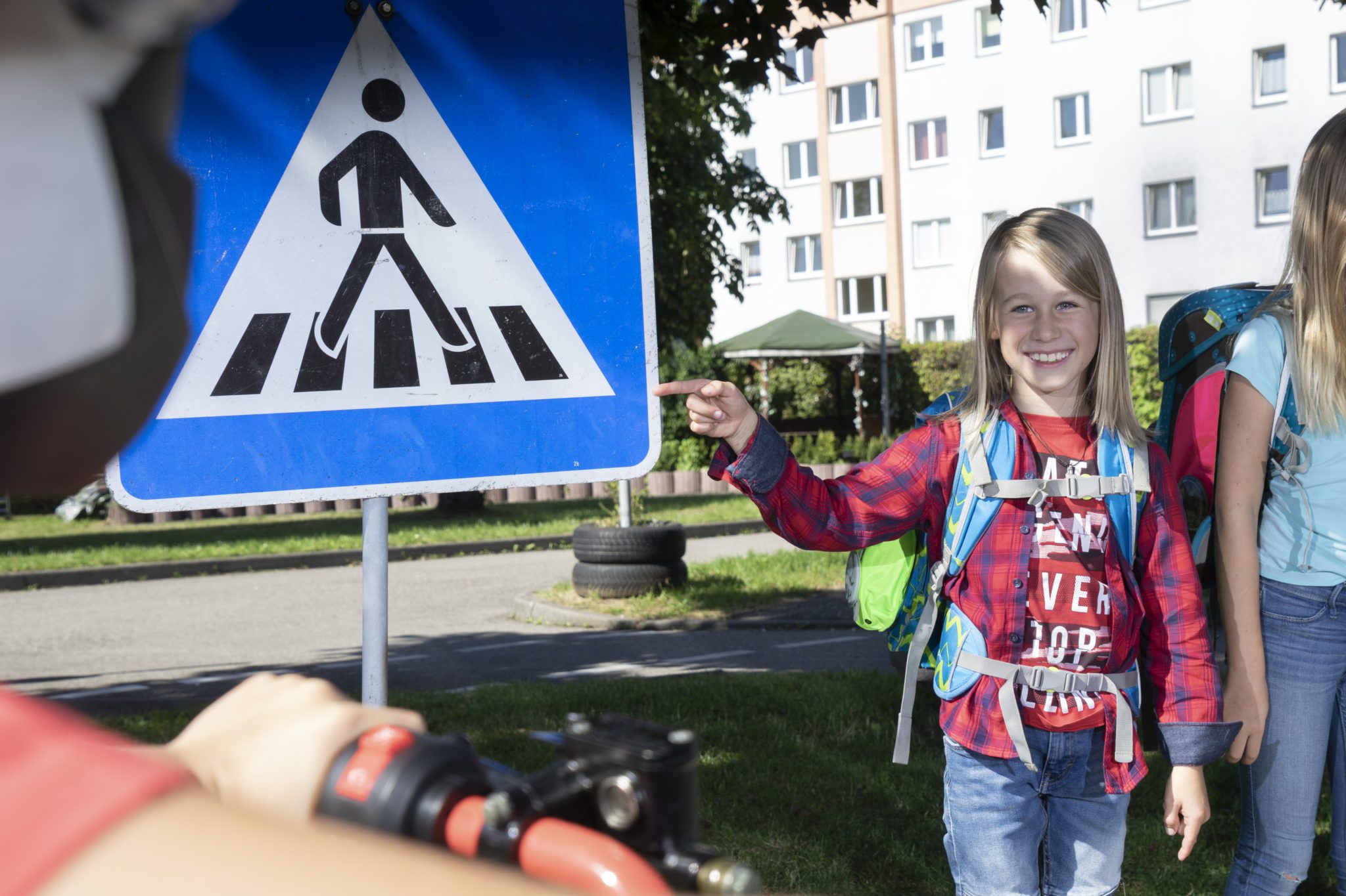 Kind am mit Schulranzen zeigt auf Zebrastreifen Schild